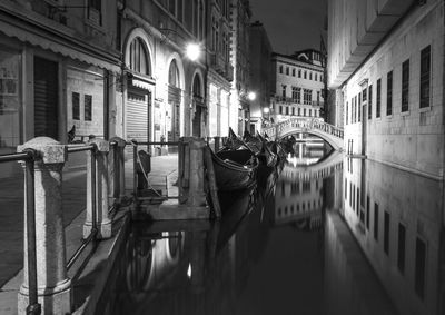 Gondolas moored in canal by buildings at night