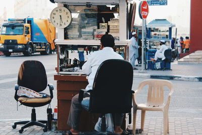 Rear view of clock repair street vendor sitting on chair