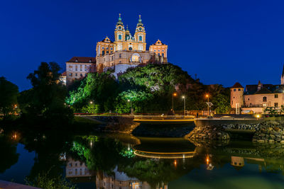 Illuminated building by river at night