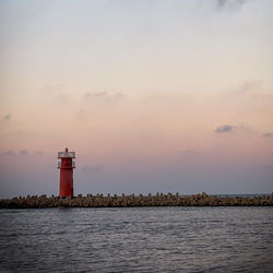Lighthouse by sea against sky during sunset