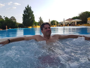 Shirtless man relaxing in swimming pool against sky