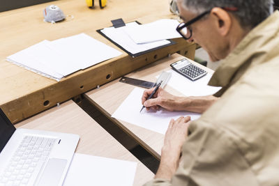 Mature man writing on paper at table in workshop