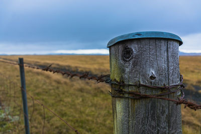 Close-up of wooden post on field against sky