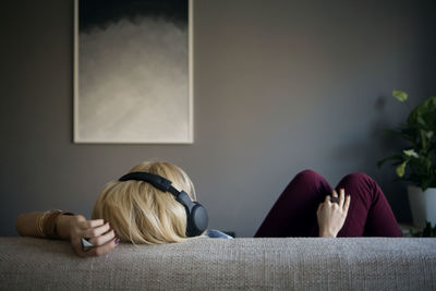 Rear view of woman listening music while lying on sofa at home