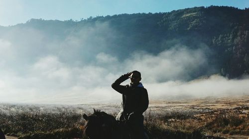 Man saluting while riding horse against fog