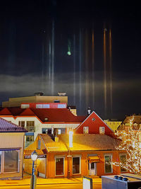 Houses by illuminated city against sky at night