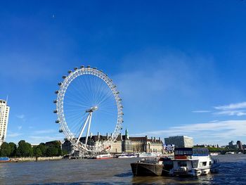 Ferris wheel by river against blue sky