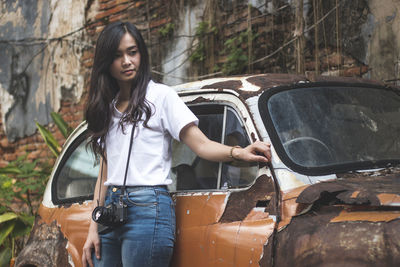 Young woman standing by abandoned car