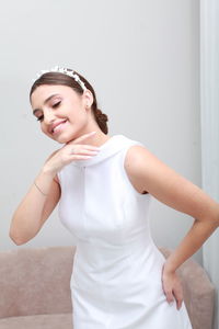 Indoor image of smiling bride in white classic dress and bridal tiara, minimalist home interior