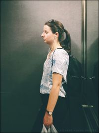 Side view of young woman looking away against wall