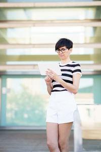 Side view of young woman using mobile phone while standing in office