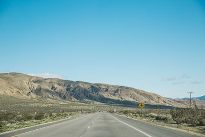 Empty road by mountains against clear blue sky