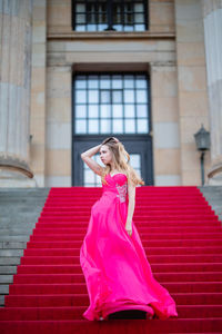 Female model wearing pink evening gown while standing on steps