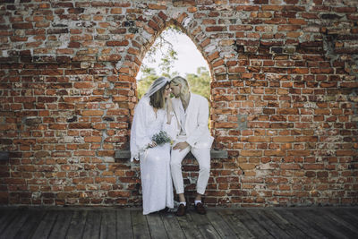 Newlywed couple sitting face to face on window during wedding