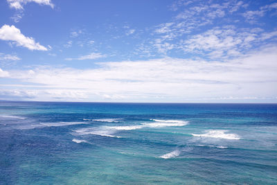 Gentle waves in a blue green ocean meeting the blue sky with scattered clouds.