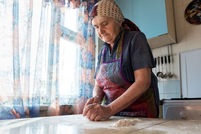 Low angle view of woman kneading dough on table at home