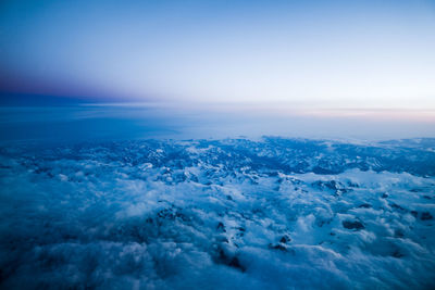 Aerial view of cloudscape over snow covered mountains by sea against blue sky