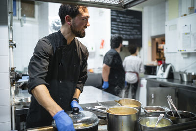 Smiling chef working with coworker taking orders in background at kitchen