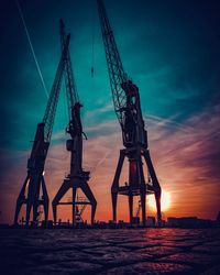 Silhouette cranes at pier against sky during sunset