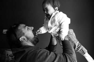 Happy father picking up son against wall at home