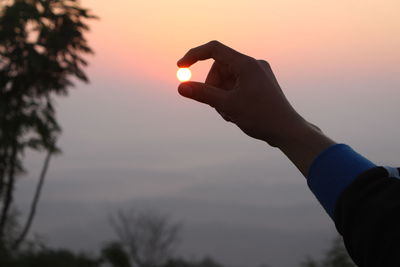 Midsection of man holding sun against sky during sunset