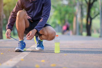 Low section of men tying shoelace while crouching on road