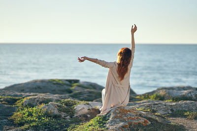 Rear view of woman sitting on rock against sky