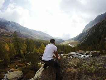 Rear view of man kneeling on rock against cloudy sky