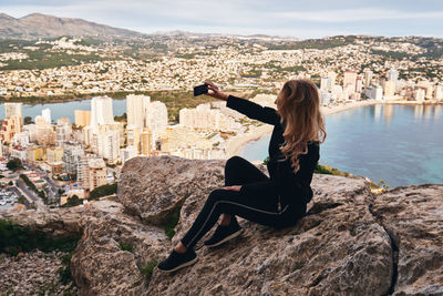 Woman taking selfie while sitting on rock