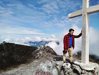 Man standing by cross on mountain against blue sky