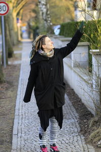 Woman touching plant while standing on footpath