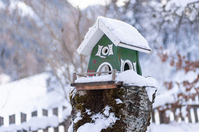 Homemade, green wooden bird's feeder in winter, under snow. blurred background.