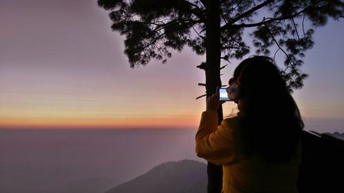 Rear view of woman photographing through mobile phone