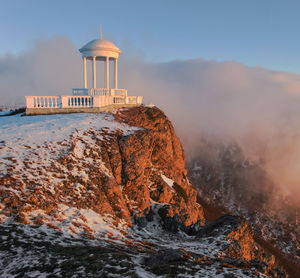 Gazebo on cliff against cloudy sky during winter