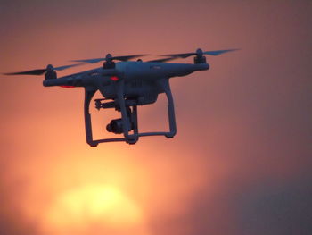 Low angle view of drone with camera flying against orange sky