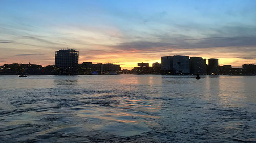 Buildings by sea against sky during sunset