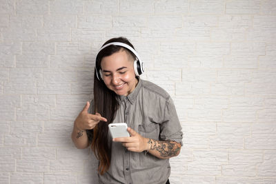 Young woman using phone while standing against wall