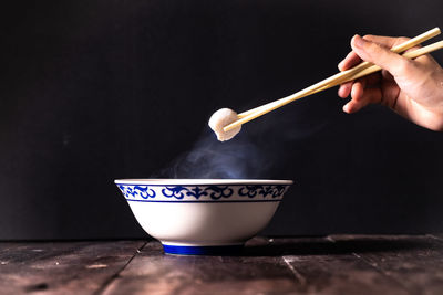 Cropped hand of person holding food with chopsticks at table