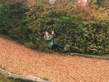 Happy woman ziplining over autumn leaves