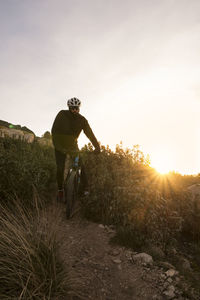 Man with bicycle on mountain against sky during sunset