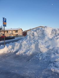 Snow covered houses by building against clear blue sky