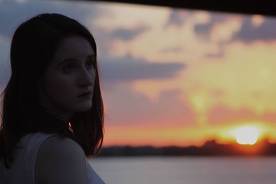 Close-up of woman by sea against sky during sunset