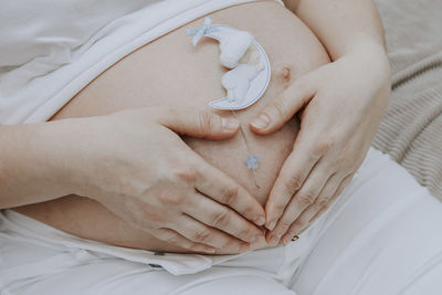 A pregnant woman holds her hands in the shape of a heart on a belly, close-up side view.