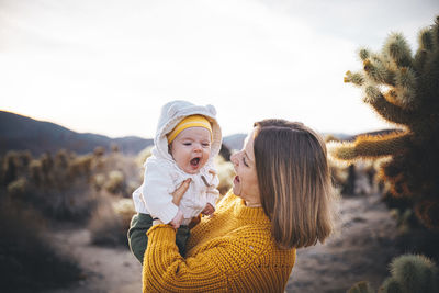 A woman with a baby is standing near a cactus in the desert