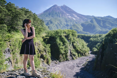 Smiling young woman standing on land against mountains and sky
