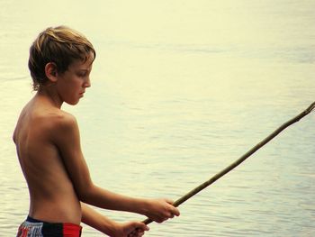 Shirtless boy holding stick against sea
