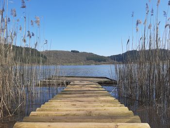 Pier over lake against clear blue sky