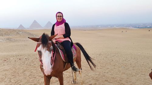Woman riding horse on pyramids sand
