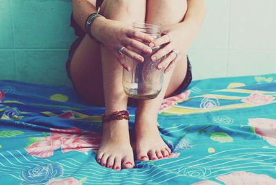 Low section of woman with empty jar sitting on bed at home