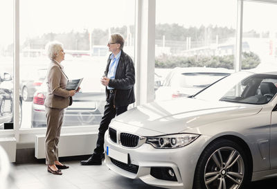 Side view of senior saleswoman discussing with man in car dealership store